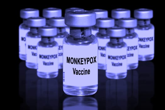 Monkeypox vaccine close-up on a black mirror background. In the background are blurred vaccine vials.