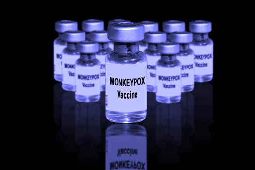 Monkeypox vaccine close-up on a black mirror background. In the background are blurred vaccine vials.