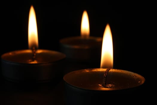 Three burning candles close-up on a black background with copy space. Blurred background.