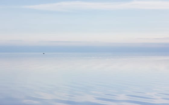 Pale lilac blue sky reflected in the calm smooth lake surface. Ethereal evening seascape in pastel colors with copy space. Atmosphere of serenity and tranquility. Russia, Vologda Oblast, Lake Beloye.