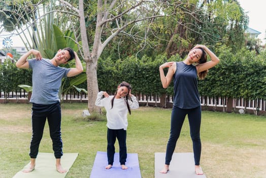 Asian young mother, father and child daughter practicing exercising stretching together before yoga workout outdoor morning in nature a field garden park. Happy family kid sport healthy lifestyle
