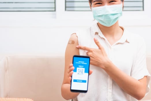 Asian young woman pointing to adhesive plaster on arm her vaccinated and showing app smartphone mobile digital screen vaccinated coronavirus (COVID-19) certificate after getting vaccine prevent