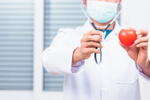 Closeup of doctor man wearing white coat standing holds his stethoscope on hand for listening examining red heart, person showing medical equipment