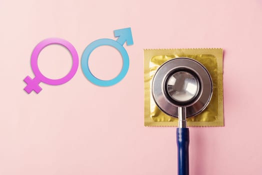 World sexual health or Aids day, Top view flat lay medical equipment, condom in pack, doctor stethoscope and Male and female gender signs, isolated on a pink background, Safe sex reproductive health