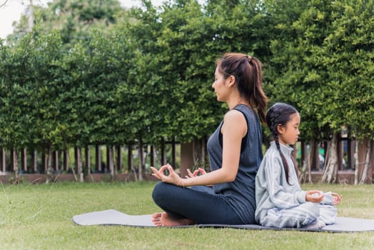 Asian young mother practicing doing yoga exercises with her daughter outdoors in meditate pose together on green grass in nature a field garden park, family sport and exercises for healthy lifestyle
