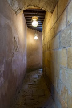 Dark vaulted stone bricks corridor with wooden ceiling leading to historical public Turkish bathhouse - Hamam Inal - illuminated with vintage Arabic glass street lanterns, Moez Street, Cairo, Egypt