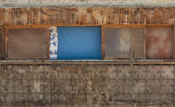 Exterior of old weathered shack with dirty windows and cloth curtains on sunny day in village