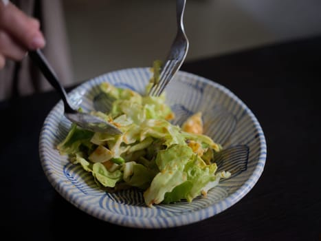 Woman mixing delicious food salad ingredients with spoons in kitchen