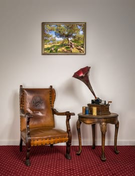 Retro ornate armchair, a 1911 old phonograph with three cylinder records on round coffee table and hanged painting on red carpet