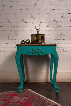 Retro composition of green vintage wooden table and old golden telephone set on a background of red carpet, dark brown wooden floor and white bricks wall