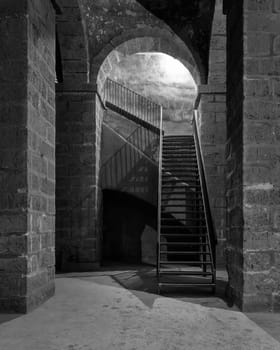 Black and white of dark abandoned underground passage with stone bricks columns and metal staircase, Medieval Cairo, Egypt