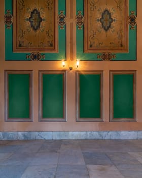 Beautiful elegant carved green frames on orange wall with ornate border and lanterns over white marble tiled floor, in abandoned old building