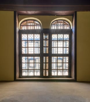 Large vintage window with ornament located inside empty room with yellow walls and wooden floor