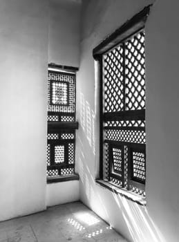 Black and white of corner of two Interleaved grunge wooden ornate windows - Mashrabiya - in stone wall at abandoned building
