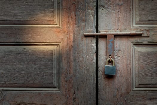 Closeup of rusted metal aged latch and padlock over weathered wooden door