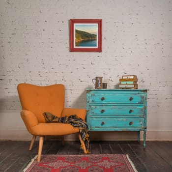 Bright orange retro armchair with plaid against white brick wall with shabby chic vintage turquoise cabinet in living room and hanged painting, with clipping path for the painting