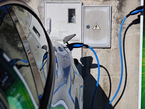 EV Car or Electric vehicle at charging station with the power cable supply plugged in on blurred nature with blue enegy power effect. Eco-friendly sustainable energy concept