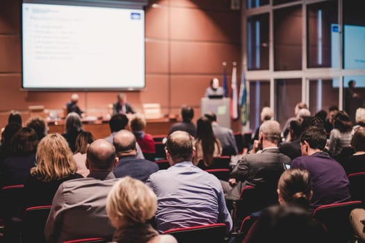 Business and entrepreneurship symposium. Speaker giving a talk at business meeting. Audience in the conference hall. Rear view of unrecognized participant in audience.