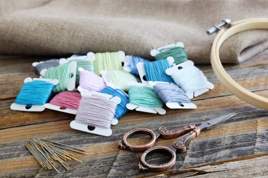 Bobbins of colorful embroidery floss with hoop and sissors on rustic wooden table.