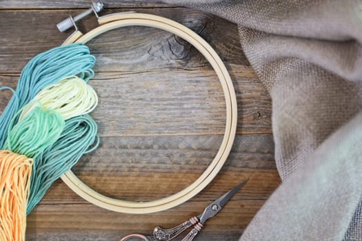 Bobbins of colorful embroidery floss with hoop and sissors on rustic wooden table. Flat lay with copy space in center of hoop