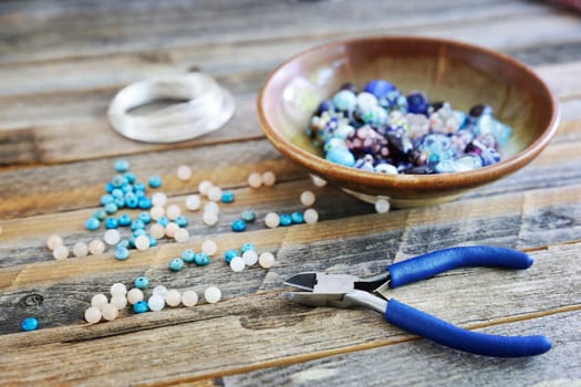 Wire cutters with glass and turquoise beads on rustic table.