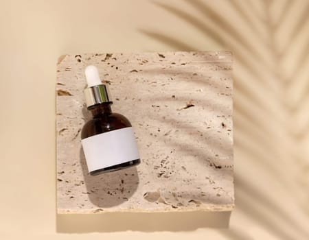 Brown Glass Dropper bottle on stone on light beige top view, packaging label mockup, Palm leaf hard shadows. Skincare beauty product, serum or lotion. Exotic natural cosmetics..