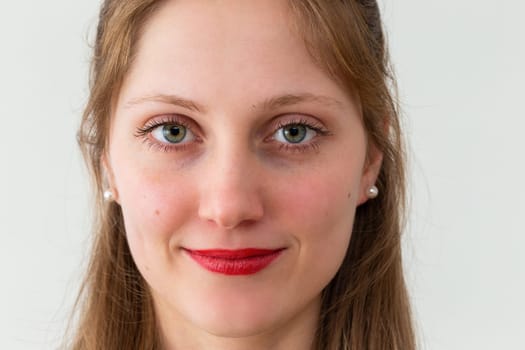 Portrait of smiling young woman looking to the camera in office with white background. Female human looking into the camera in horizontal composition.