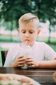 Little Boy Drinking Milkshake In Cafe In Summer Day.