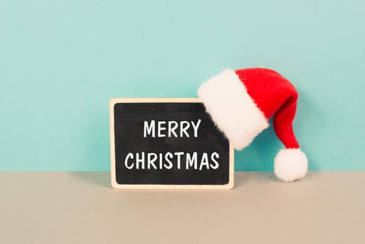 Red Santa Claus hat hanging on a chalkboard, greeting card with merry christmas wishes, winter season