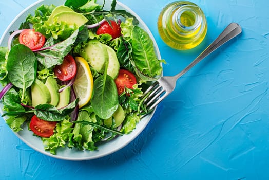 Healthy green salad with avocado and fresh vegetables on blue table close up