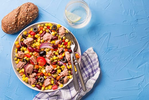 Healthy mixed tuna salad with corns, carrots, peas, beans and olives on blue table background. Mexican corn salad.