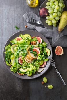 Fresh green leafy salad with fruits and nuts on dark table background. Concept for a tasty and healthy meal