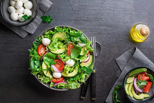 Healthy green salad with avocado mozzarella cheese and fresh vegetables on dark background