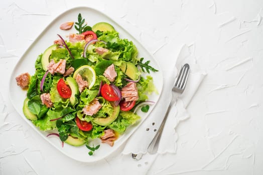 Fresh green leafy salad with tuna avocado and tomato on white table background. Concept for a tasty and healthy meal