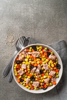 Healthy tuna salad with corns, carrots, peas, and olives on grey table background. Mexican corn salad.