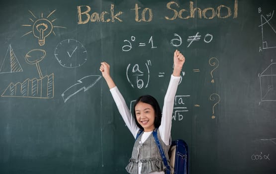 Education Back to school. Asian school girl in uniform on classroom raised arms to successful finished homework, primary child is standing front of class in school raised hands in win position