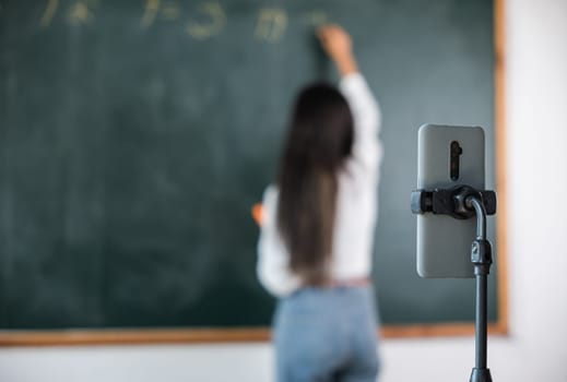 Back to school online class. Asian teacher teach on board while have blackboard lecture online through smartphone in classroom, woman standing front of class live video call online smart mobile phone