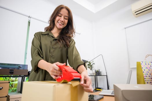 Asian young woman hand packing shipment box with transparency tape at home office, happy freelance and packing cardboard box delivery products to customers, Startup small business, Moving day