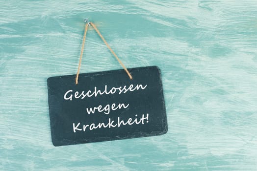 The words closed because of illness are standing in german language on a chalkboard sign, hanging on a blue textured weathered door, concept for business, stores and restaurants