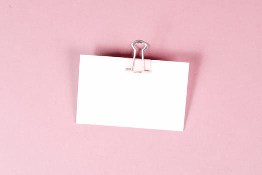 Blank white paper with a paperclip on a pink colored background, copy space for text, reminder or message in the office, communication concept