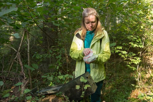 A woman in woods finds a large geocaching container.
