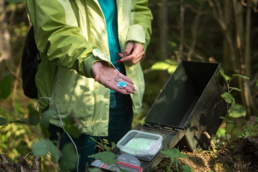A woman in woods finds a large geocaching container.