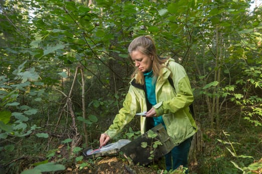 A woman in woods finds a large geocaching container.