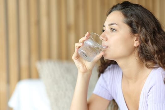 Relaxed woman drinking tap water from glass in a bedroom
