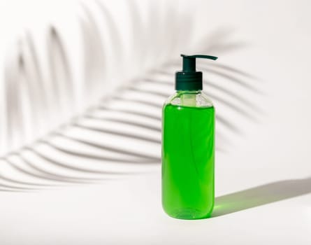Refillable Cosmetic pump dispenser bottle filled with green liquid on white, Palm leaf hard shadows, close up, mockup. Skincare beauty product, facial cleaner or lotion. Natural cosmetics..