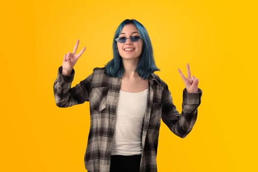 Smiling young woman student with blue hair doing positive gestures with her hands isolated over yellow background
