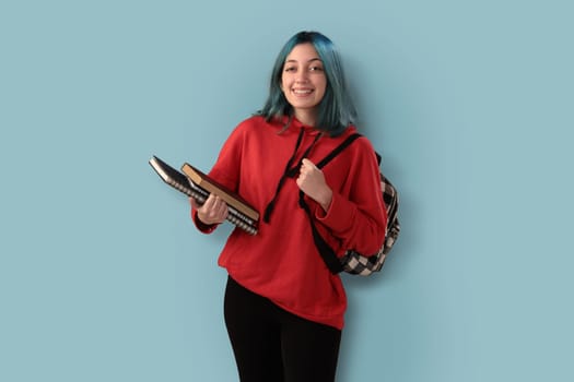 Cute young gilr student with blue hair books and a backpack over a cyan background