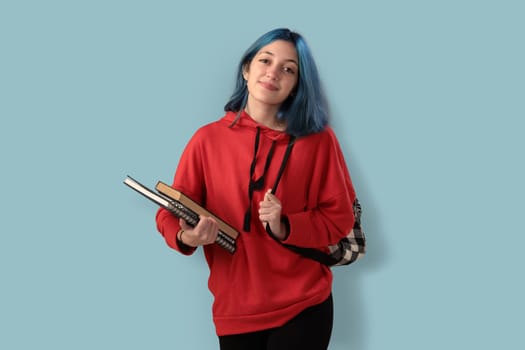 Cute young gilr student with blue hair books and a backpack over a cyan background