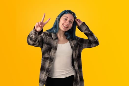 Smiling young woman student with blue hair doing positive gestures with her hands isolated over yellow background