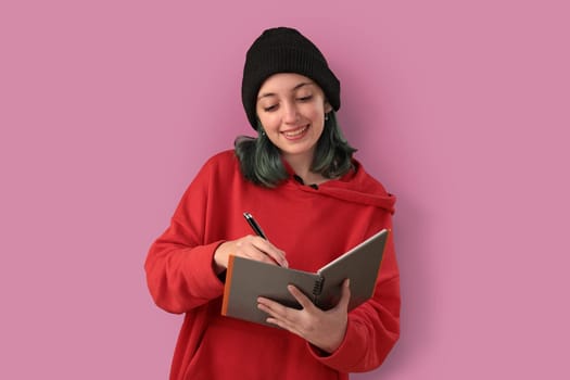 Cute young girl with blue hair taking notes over a pink background